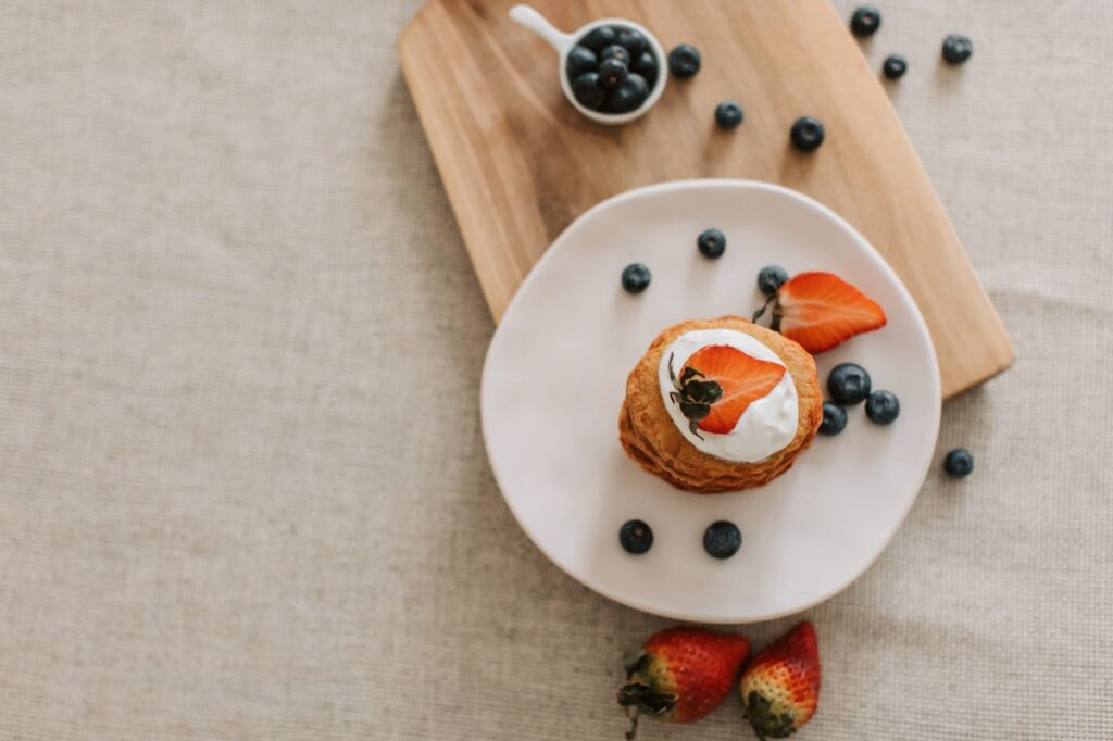 pexels-photo-6947242 A tasty dessert with whipped cream, strawberries, and blueberries on a wooden board.